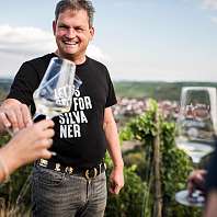 MainGenussTrail c hannes niederkofler web 5556 Ralph Düker mit einem Glas Weisswein vor dem Weinberg